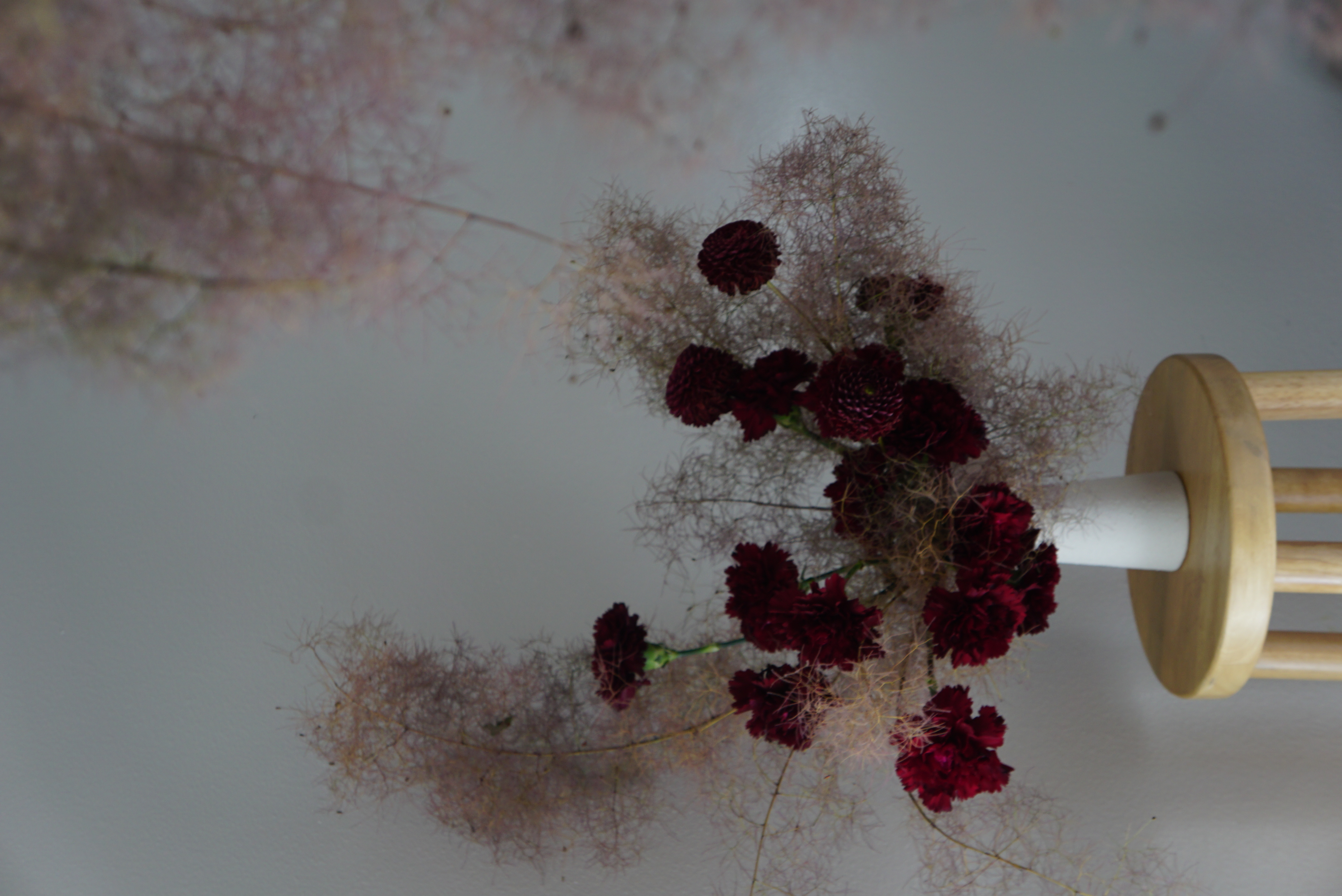 A sculptural flower arrangement of smokebush plumes and deep red carnations in a tall compote vase.