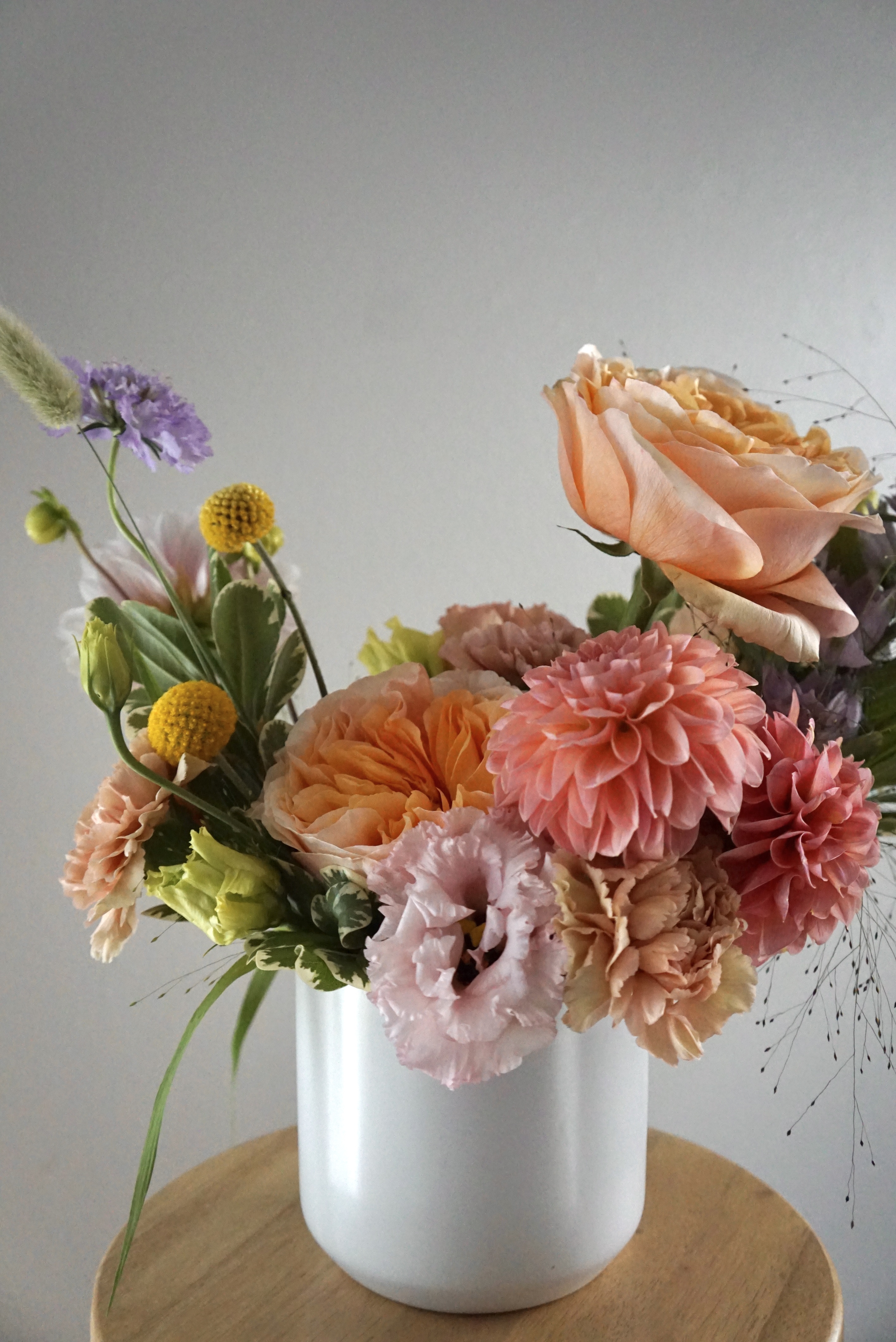 A classic flower arrangement with a mix of peach roses, pink dahlias, pink lisianthus, purple scabiosas, peachy carnations, yellow billy balls, explosion grass and bunny tail grass.